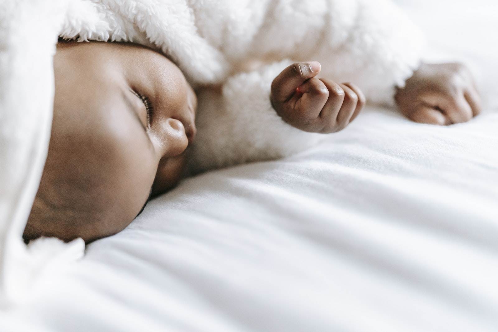 Adorable ethnic newborn baby in soft warm clothes sleeping on comfortable bed in daylight
